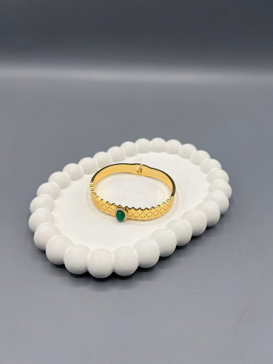 This is a gold-plated bangle-style bracelet with a green gemstone or zircon.