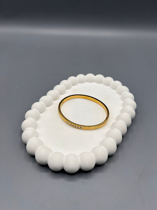 This is a hinged gold bangle bracelet with seven studded zircon stones.