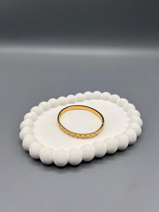 This is an 18k gold-plated stainless steel bangle bracelet with cubic zirconia stones.