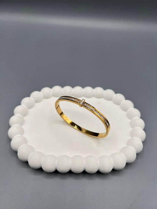 This is a gold-plated bangle bracelet with cubic zirconia stones.